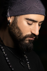 Dark close up portrait of a man with piercings and bandana.