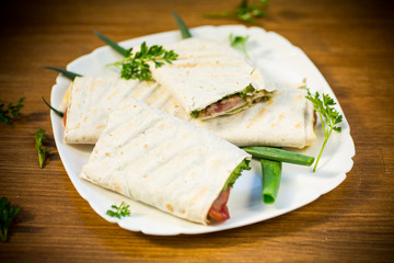 Fototapeta na wymiar roll of pita with lettuce leaves, greens and sausage in a plate