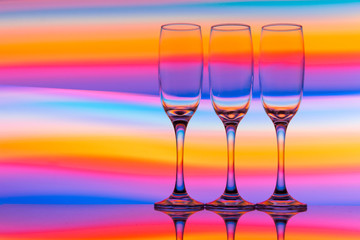 Three champagne glasses / flutes in a row with colorful multicolored light painting behind them
