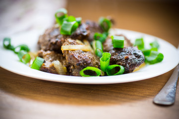 fried liver with onions in a plate on a wooden