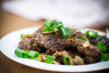 fried liver with onions in a plate on a wooden