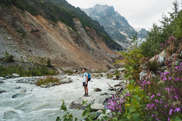 Fototapeta na wymiar male traveler looking at flashy stream flowing in mountain valley 