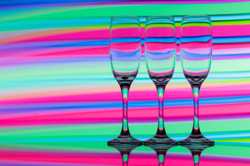 Three champagne glasses / flutes in a row with colorful multicolored light painting behind them
