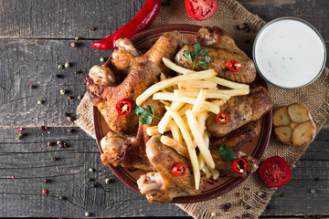 Close-up photo of bbq chicken wings with fries and beer. Barbeques meat with sauces, ketchup, mayonnaise. Fast and junk food concept. 