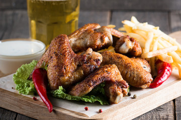Close-up photo of bbq chicken wings with fries and beer. Barbeques meat with sauces, ketchup, mayonnaise. Fast and junk food concept. 