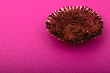 Empty chocolate muffin wrapper on a pink background