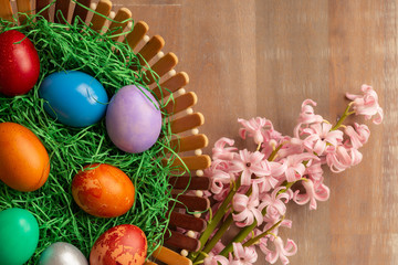 Top view of colorful easter eggs in basket with flowers by side
