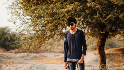 Indian man wearing sunglasses posing in front of the tree