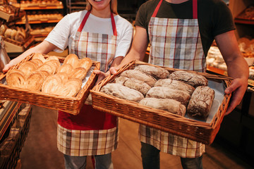 Young man and woman hold baskets of fresh tasty white dark bread in hands. Stand in grocery store....