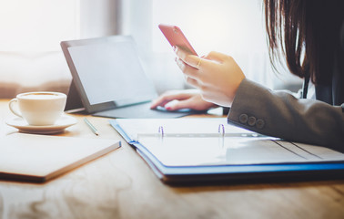 Fototapeta premium Closeup of hand asian businesswoman holding smartphone and working with laptop on wooden table in cafe. Background vintage light. soft focus and blur