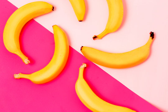 Colorful fruit pattern of fresh yellow bananas on pink and pastel blue background. From top view
