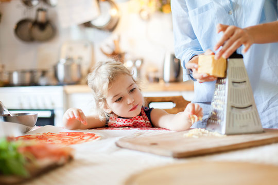 Funny Kid Gourmet Is Eating And Tasting Cheese. Family Are Cooking Pizza And Preparing Homemade Italian Food And Meal In Kitchen. Cute Little Girl Is Helping Mother. Children Chief-cooker Concept.