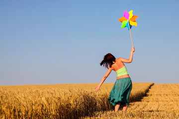 Young woman with pinwheel toy on wheat field.