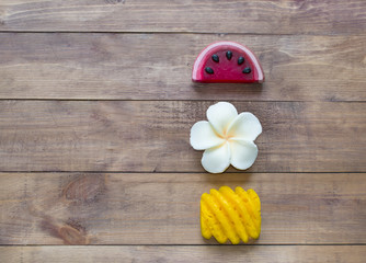 Hand made soap in the shape of fruit yellow pineapple, watermelon and flower on wooden background.