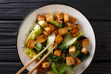 Traditional fried tofu with bok choy, soy sauce and sesame close-up on a plate. Horizontal top view