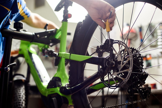 Cropped shot of male mechanic working in bicycle repair shop, serviceman repairing modern bike brakes using special tool, wearing protective workwear
