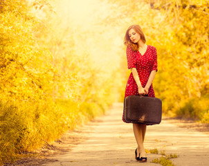Redhead girl with suitcase at tree's alley.