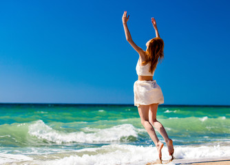 Young redhead girl jumping at the beach.