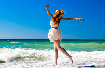 Young redhead girl jumping at the beach.