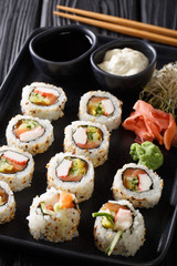 Fresh Japanese rolls uramaki served with sauces, ginger and wasabi closeup on a plate. vertical