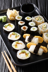  large set of Japanese rolls such as Hosomaki, Uramaki, Maki, Nigiri, Tamagoyaki served with ginger, wasabi and soy sauce close-up on a plate. vertical
