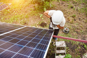 View from above of technician working with screwdriver connecting solar photo voltaic panel to exterior metal platform on sunny day. Alternative renewable ecological green energy sources concept.