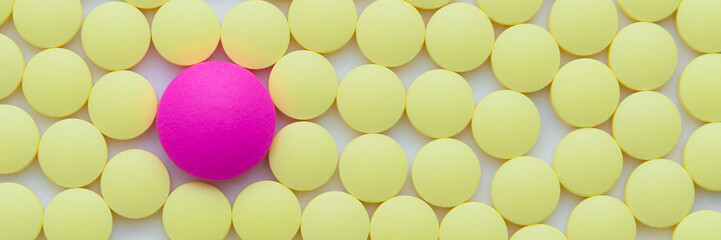 Small yellow and one pink pills on a white background close-up.