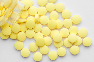 Yellow pills scattered from a glass jar on a white background.