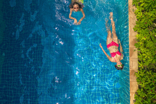 aerial top view above swimming pool. woman in yellow bikini and woman in red bikini are swimming .in villa pool