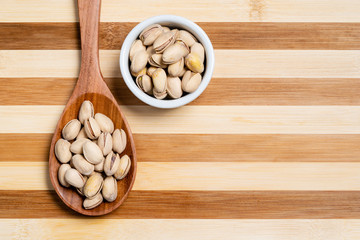Pistachio in wooden spoon and bamboo striped dessert pot.