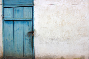 Old padlock. The door is wooden painted in blue. The wall is white, covered with lime.Background.