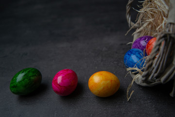 Multi-colored painted Easter eggs in a basket on a dark stone background. Happy Easter holiday card or banner. Copy space.