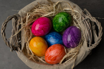 Multi-colored painted Easter eggs in a basket on a dark stone background. Happy Easter holiday card or banner. 