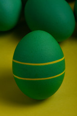 One green painted Easter egg with two yellow stripes stands in front of green eggs on a yellow background. Happy Easter holiday card or banner.