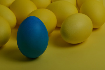 One blue painted Easter egg stands in front of yellow eggs on a yellow background. Happy Easter holiday card or banner.