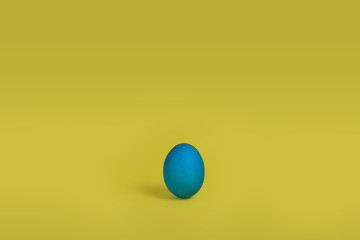 One blue painted Easter egg stand on a yellow background. Happy Easter holiday card or banner. Copy space.