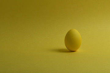 One yellow painted Easter eggs stand on a yellow background. Happy Easter holiday card or banner. Copy space.