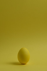 One yellow painted Easter eggs stand on a yellow background. Happy Easter holiday card or banner. Copy space.