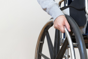 Detail of disabled woman holding a hand on wheel of a wheelchair.