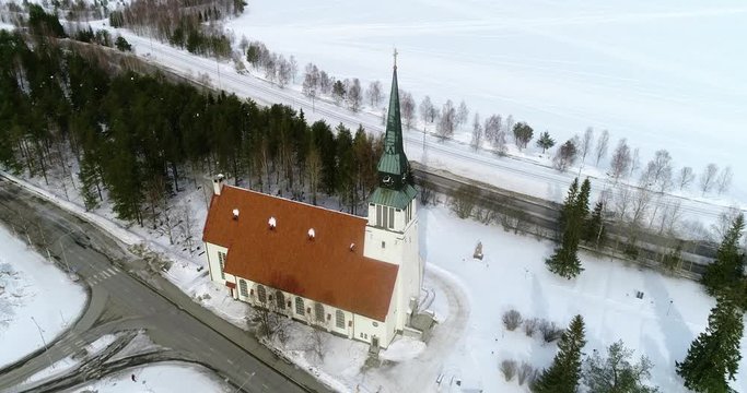 Aerial, tilt up, drone shot, over Kemijarvi village church, overlooking a lake and northern wilderness, on a cloudy, winter day, at the arctic circle, in Lapland, north Finland