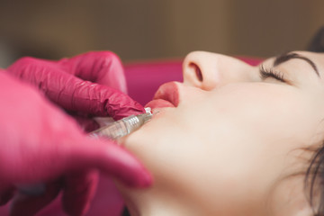 Cosmetologist making an ingection to her client. Woman beauty procedure, lip augmentation...