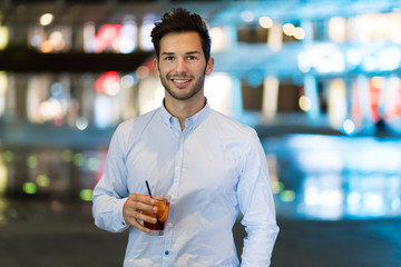 Young man holding a drink at a night club outdoor