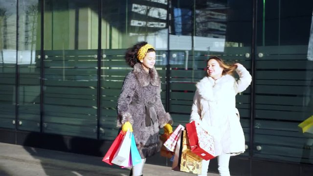 Two girls with purchases in their hands are standing on street near shop window