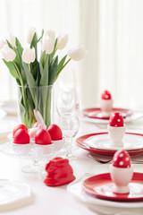 Happy easter. Decor and table setting of the Easter table is a vase with white tulips and dishes of red and white color. Easter colored eggs with white polka dots.