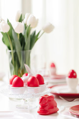 Happy easter. Decor and table setting of the Easter table is a vase with white tulips and dishes of red and white color. Easter colored eggs with white polka dots.
