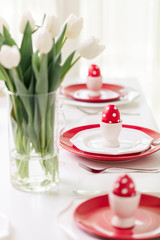 Obraz na płótnie Canvas Happy easter. Decor and table setting of the Easter table is a vase with white tulips and dishes of red and white color. Easter colored eggs with white polka dots.