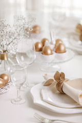 Happy Easter! Golden decor and table setting of the Easter table with white dishes of white color.