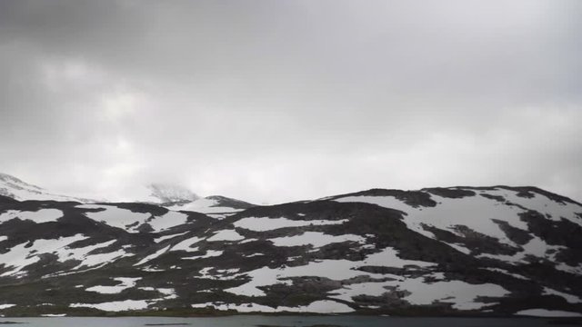 Pan right of mountain panorama from the Gamle Strynefjellsvegen Riksvei 258 in Oppland and Sogn og Fjordane, Norway, with snow and ice covered mountains, the glacier lake Langvatnet and a cloudy sky.