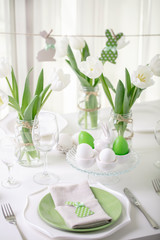 Decor and table setting of the Easter table with white tulips and dishes of green and white color. Easter decor in the form of Easter bunnies  green color with white polka dots.
