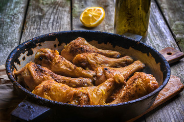 Roasted chicken drumsticks in frying pan, close up view